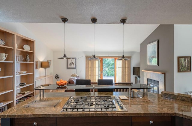 kitchen featuring lofted ceiling, stainless steel gas stovetop, decorative light fixtures, and a fireplace