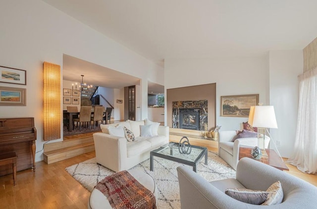 living room with a high end fireplace, vaulted ceiling, light hardwood / wood-style flooring, and a notable chandelier