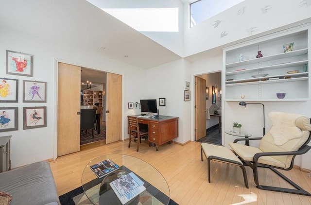 office space featuring a towering ceiling, a chandelier, and light wood-type flooring