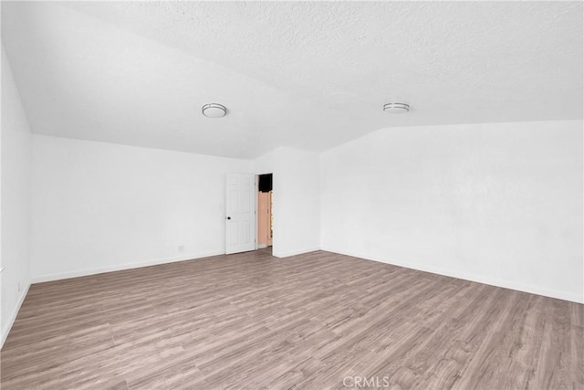 spare room featuring lofted ceiling, a textured ceiling, and light hardwood / wood-style floors