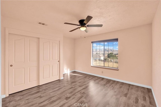 unfurnished bedroom featuring a textured ceiling, wood-type flooring, a closet, and ceiling fan