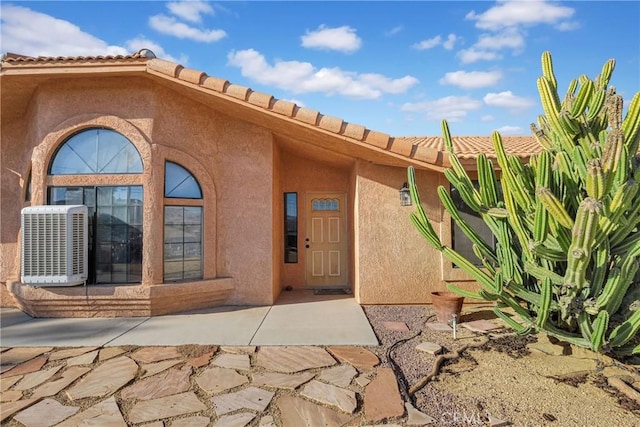 view of exterior entry featuring central AC and a patio area