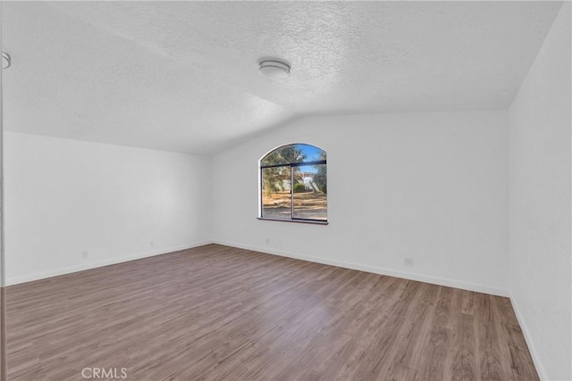 additional living space featuring hardwood / wood-style floors, vaulted ceiling, and a textured ceiling