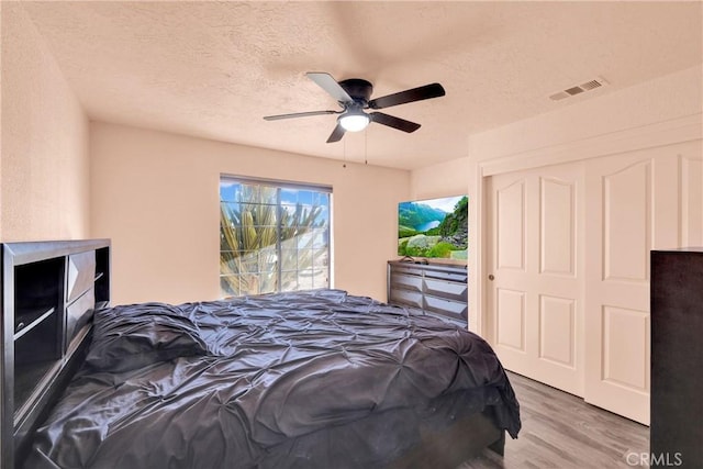 bedroom featuring hardwood / wood-style flooring, a closet, ceiling fan, and a textured ceiling