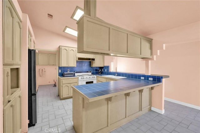 kitchen with sink, white range with gas stovetop, refrigerator, tile countertops, and kitchen peninsula