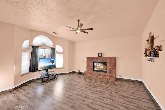 unfurnished living room with lofted ceiling, a brick fireplace, a textured ceiling, ceiling fan, and hardwood / wood-style floors