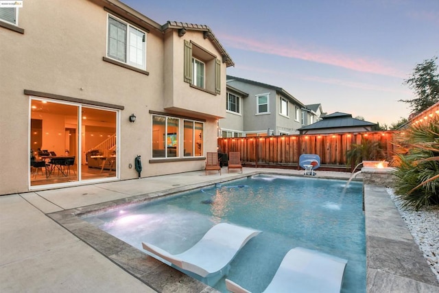 pool at dusk with pool water feature and a patio area