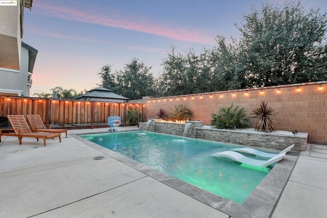 pool at dusk featuring a patio area and pool water feature