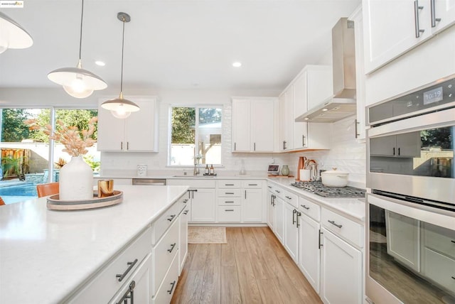 kitchen featuring pendant lighting, stainless steel appliances, ventilation hood, and white cabinets