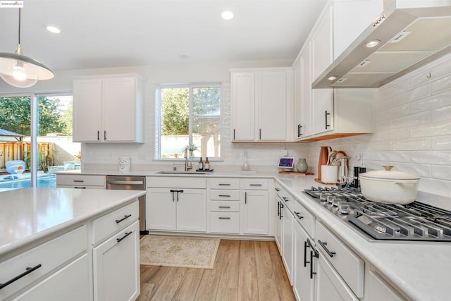 kitchen with appliances with stainless steel finishes, white cabinetry, sink, wall chimney range hood, and light hardwood / wood-style flooring