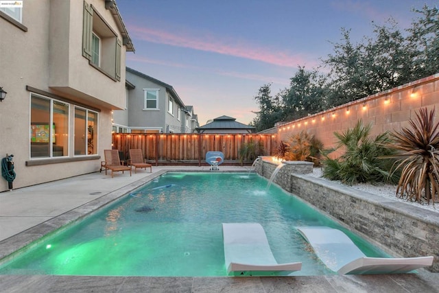 pool at dusk with a patio and pool water feature