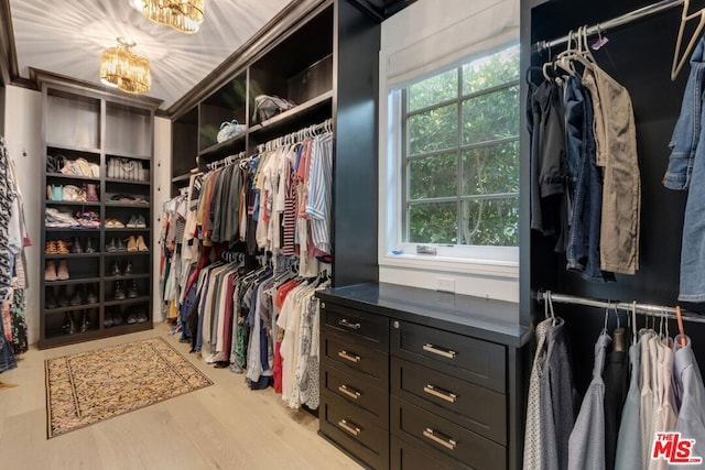 spacious closet featuring an inviting chandelier and light hardwood / wood-style flooring