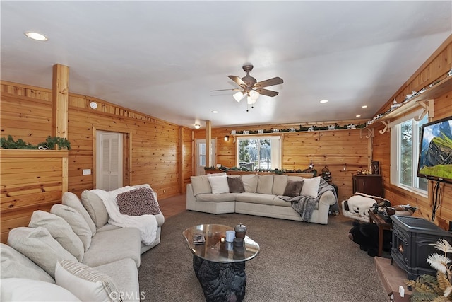 living room with ceiling fan, carpet floors, a wood stove, and wood walls