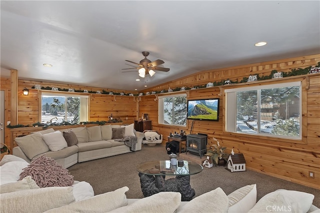 carpeted living room with lofted ceiling, a wood stove, ceiling fan, and wood walls