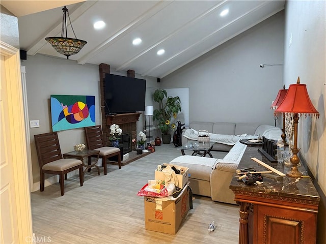 living room featuring vaulted ceiling with beams, light hardwood / wood-style floors, and a brick fireplace