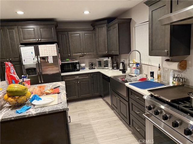 kitchen featuring sink, light hardwood / wood-style flooring, appliances with stainless steel finishes, dark brown cabinetry, and wall chimney exhaust hood