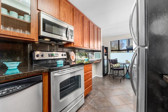 kitchen with backsplash, stainless steel appliances, dark stone counters, and dark tile patterned floors