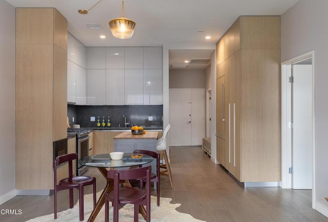 kitchen featuring hanging light fixtures, light wood-type flooring, stainless steel stove, decorative backsplash, and white cabinets