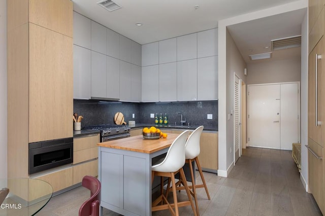 kitchen featuring a breakfast bar, wooden counters, stainless steel stove, a kitchen island, and decorative backsplash