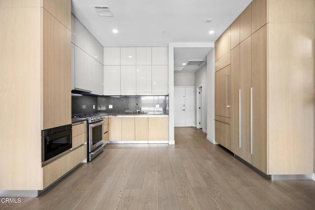 kitchen with light brown cabinetry, black microwave, sink, decorative backsplash, and high end stainless steel range oven