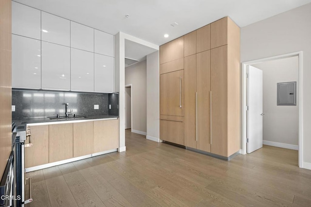 kitchen featuring sink, electric panel, white cabinets, and light brown cabinets