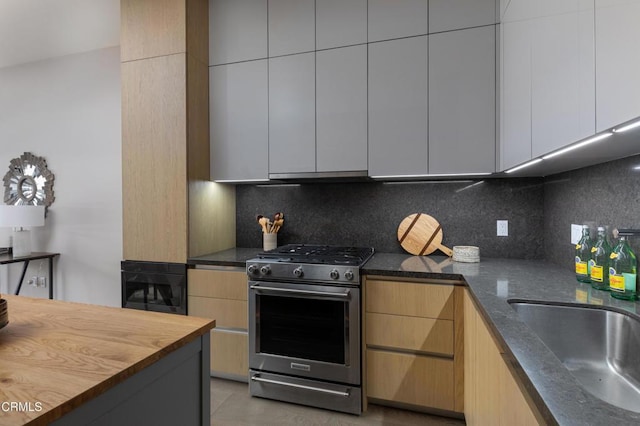 kitchen with butcher block countertops, sink, stainless steel gas range oven, tasteful backsplash, and range hood