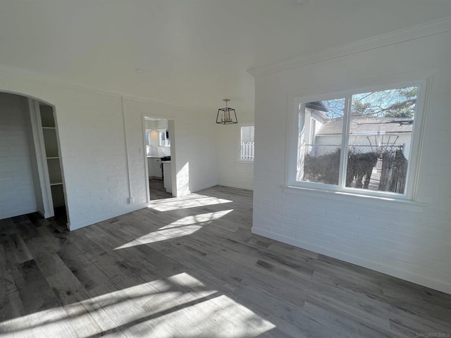 unfurnished living room featuring dark wood-type flooring, brick wall, and crown molding