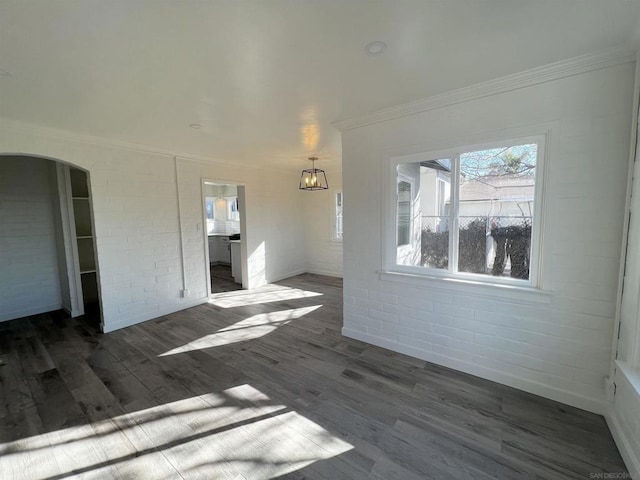 unfurnished living room featuring dark hardwood / wood-style flooring, ornamental molding, and brick wall