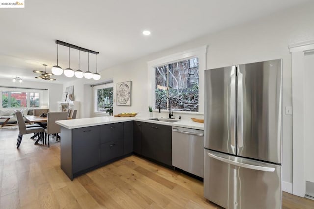 kitchen with sink, hanging light fixtures, light hardwood / wood-style flooring, kitchen peninsula, and stainless steel appliances