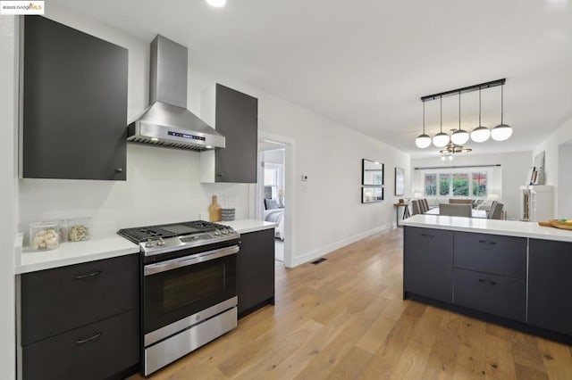 kitchen featuring wall chimney range hood, stainless steel gas range, light wood-type flooring, and decorative light fixtures