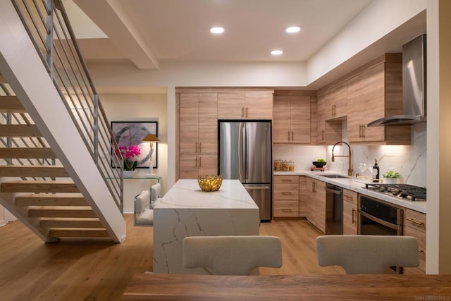 kitchen with wall chimney range hood, light hardwood / wood-style flooring, sink, and appliances with stainless steel finishes