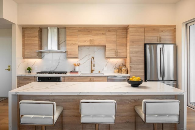 kitchen featuring wall chimney range hood, sink, a breakfast bar area, stainless steel appliances, and decorative backsplash