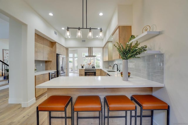 kitchen featuring sink, a breakfast bar area, stainless steel appliances, island range hood, and kitchen peninsula