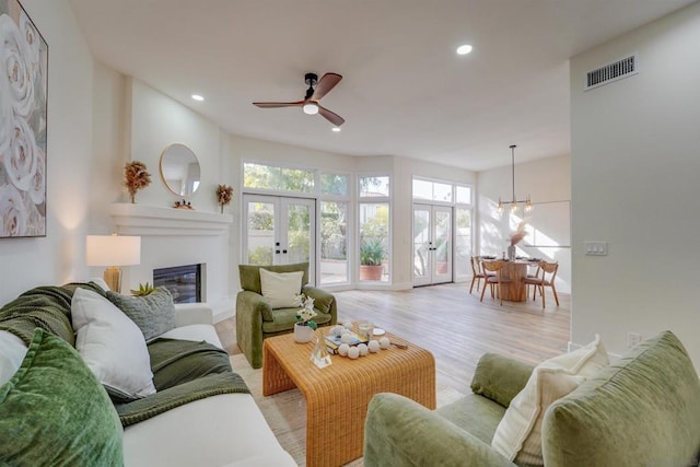 living room featuring french doors, ceiling fan with notable chandelier, and light hardwood / wood-style flooring