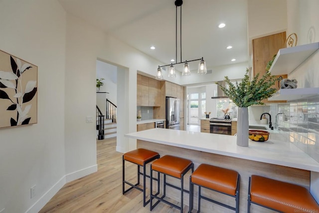 kitchen featuring light hardwood / wood-style flooring, a kitchen bar, stainless steel fridge with ice dispenser, decorative light fixtures, and kitchen peninsula