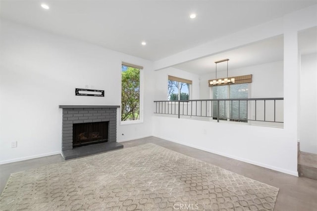 unfurnished living room with an inviting chandelier, a brick fireplace, and concrete floors