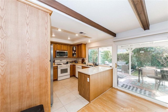 kitchen featuring sink, beam ceiling, stainless steel appliances, a tray ceiling, and kitchen peninsula