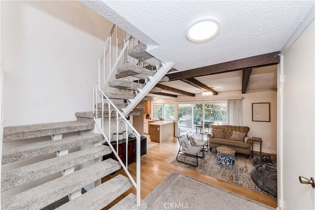 stairs with hardwood / wood-style floors, a textured ceiling, and beamed ceiling