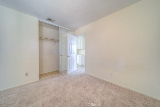 unfurnished bedroom with light colored carpet and a closet