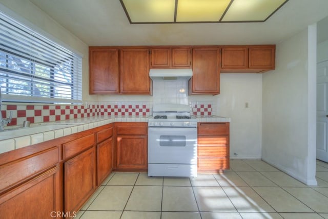 kitchen with light tile patterned floors, backsplash, tile countertops, and white gas range oven