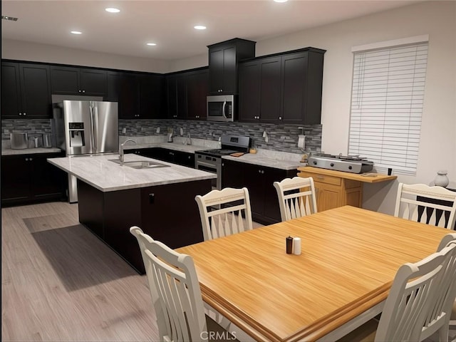 kitchen featuring appliances with stainless steel finishes, sink, decorative backsplash, a center island with sink, and light wood-type flooring