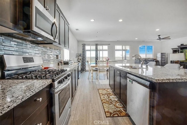 kitchen featuring light stone counters, a sink, light wood-style floors, appliances with stainless steel finishes, and a center island with sink