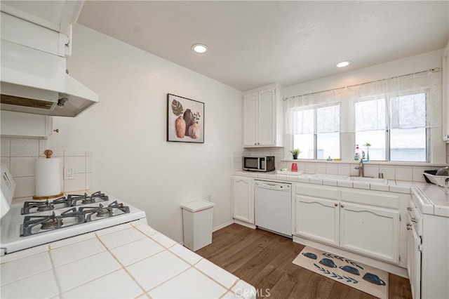 kitchen with backsplash, tile countertops, dishwasher, and white cabinets