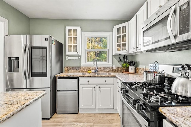 kitchen featuring white cabinetry, appliances with stainless steel finishes, sink, and light stone counters