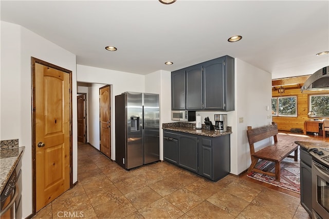 kitchen featuring gray cabinets, appliances with stainless steel finishes, dark stone counters, and range hood