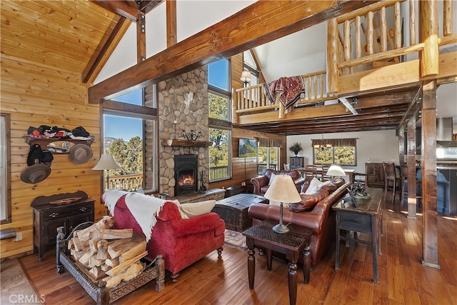 living room featuring wooden walls, a fireplace, wood-type flooring, a notable chandelier, and beam ceiling