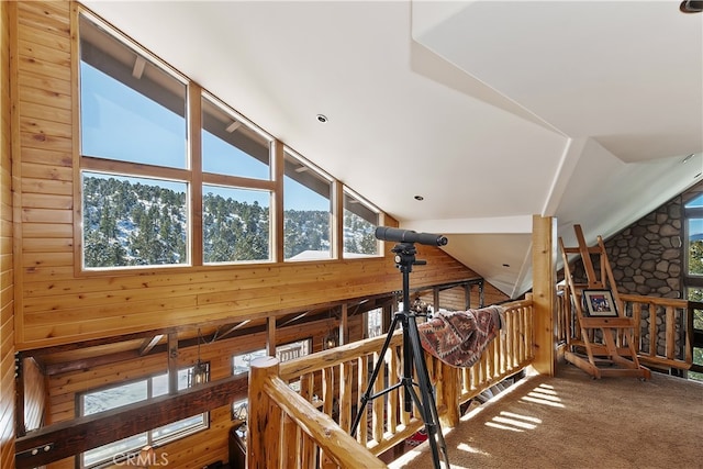 hall featuring carpet flooring, vaulted ceiling, and wood walls