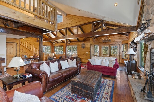 living room with dark wood-type flooring, beam ceiling, wooden walls, a notable chandelier, and a fireplace