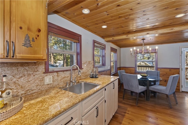 kitchen with sink, hanging light fixtures, light stone counters, white cabinets, and wooden ceiling