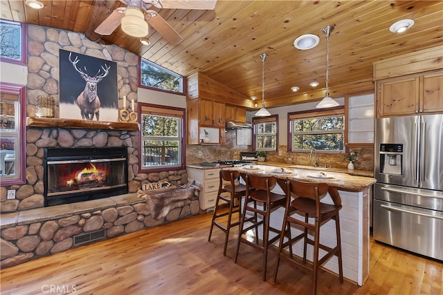 kitchen with sink, light stone counters, decorative light fixtures, a center island, and stainless steel fridge